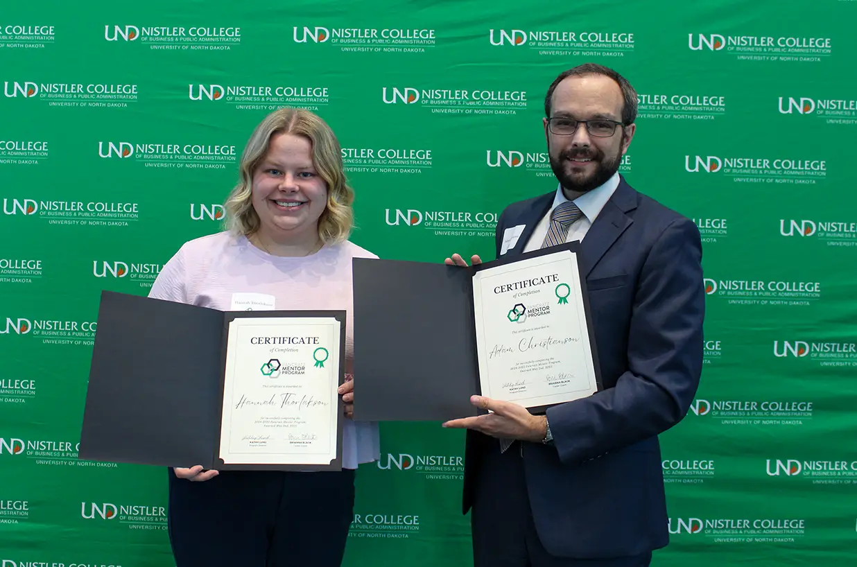 Hannah and Adam posing with completion certificates by UND background