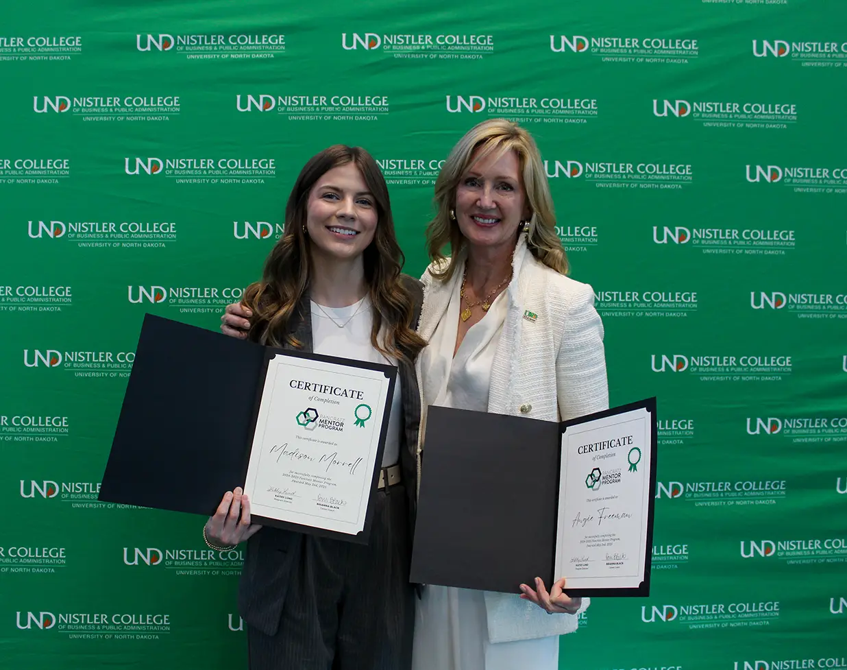 Madi and Angie posing with completion certificates by UND background
